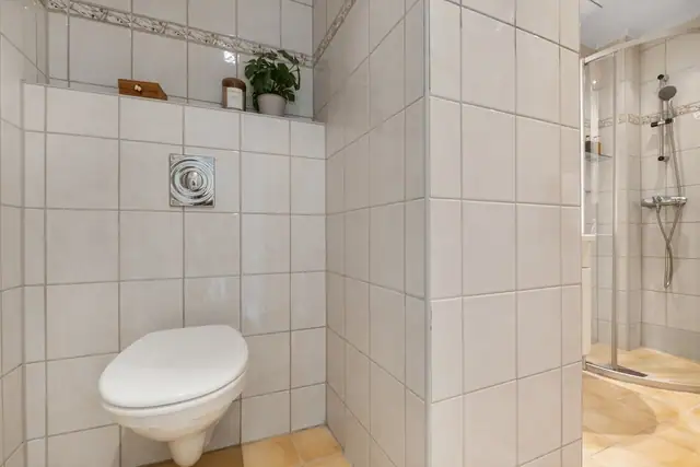 Rommet er utstyrt med dusjhjørne med skyvedører, veggmontert toalett samt servantskap med hvit servant og tilhørende blandebatteri