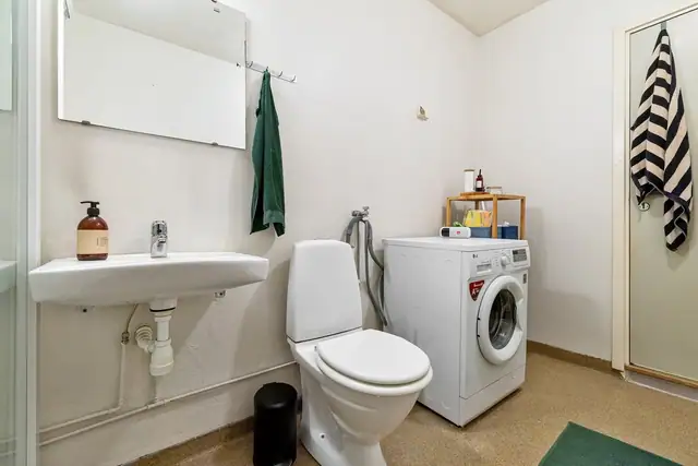 Badet er utstyrt med dusjkabinett, gulvmontert toalett, hvit servant med Oras-blandebatteri.