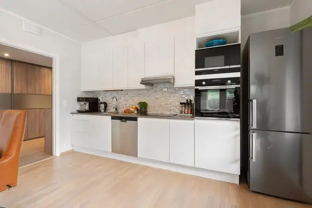 Pent Aubo-kjøkken med glatte fronter og innfelte håndtak. Kjøkkenet har laminert benkeplate med oppvaskkum i rustfritt stål og svingbart blandebatteri.